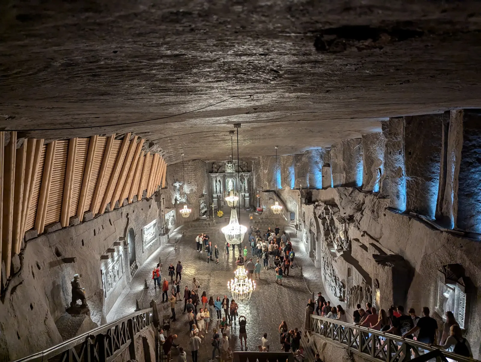Visitors descending a staircase into the vast underground chamber of St. Kinga's Chapel, lit by chandeliers beneath a rock-salt ceiling