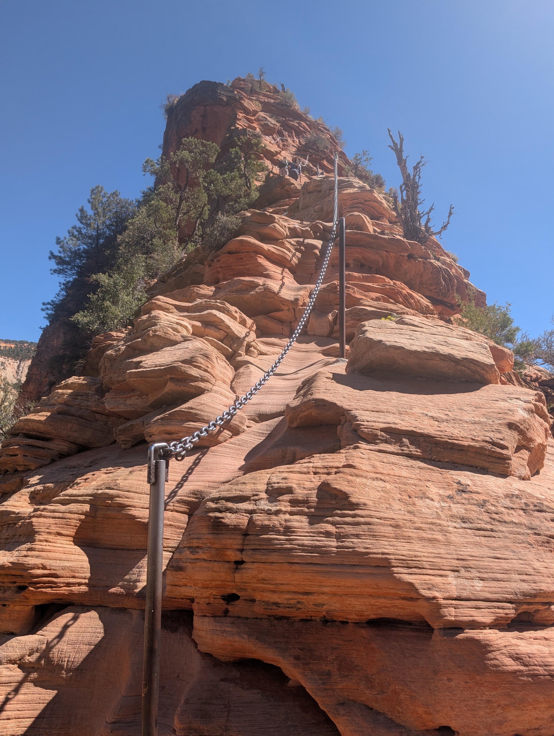 A chain strung between metal posts along a narrow bare-rock ridge, with sheer red canyon walls dropping away on both sides
